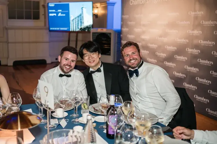 Three guests in dinner jackets smiling together at their table at the Chambers High Net Worth Awards 2025.