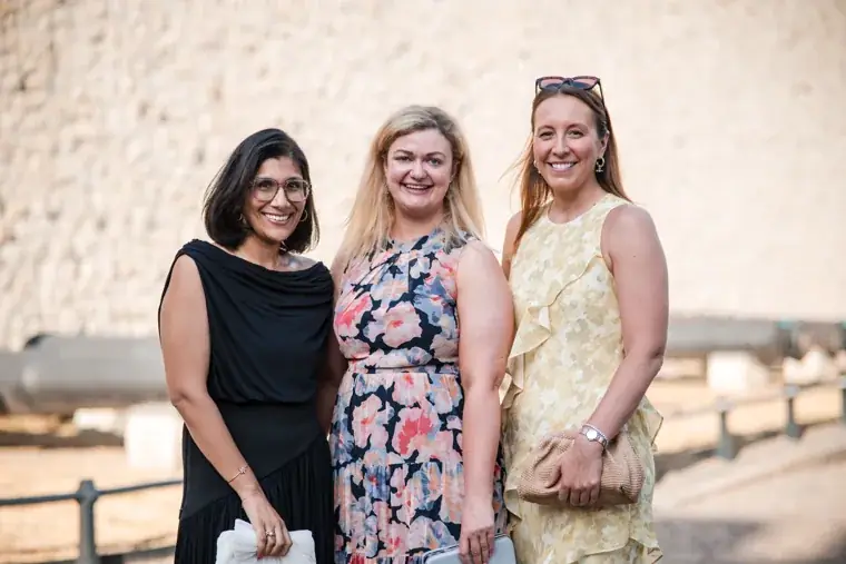 Three guests posing together beside the sunlit stone wall at the Chambers High Net Worth Awards 2025.