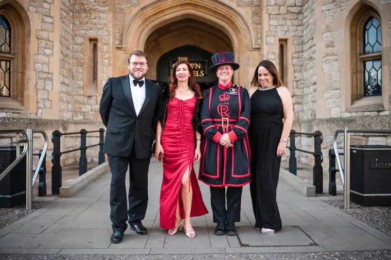 Three guests posing with a Yeoman Warder beneath a stone arch at the Chambers High Net Worth Awards 2025.
