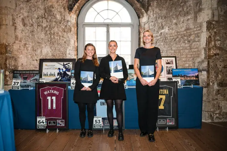Three guests standing beside a display of framed artwork at the Chambers High Net Worth Awards 2025.
