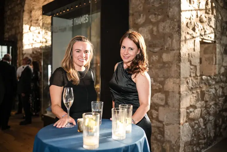 Two guests posing at a tall table beside the stone wall at the Chambers High Net Worth Awards 2025.