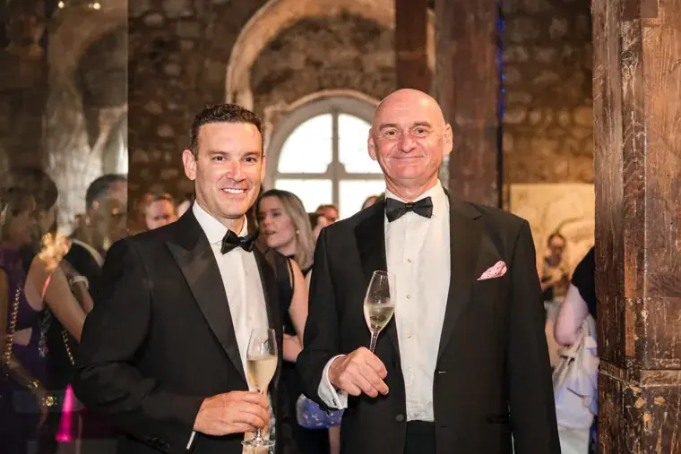 Two smiling guests posing with drinks beside a window at the Chambers High Net Worth Awards 2025.