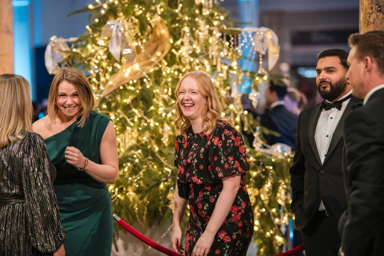Two women laughing beside the decorated tree at the Chambers UK Awards winter edition.