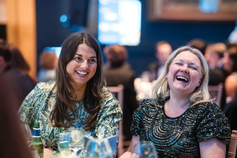 Two women laughing together at the dinner table at the Chambers UK Awards winter edition.
