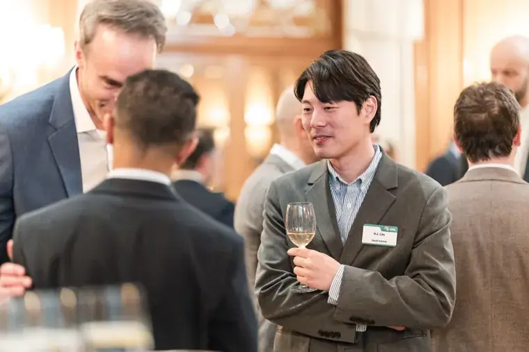 A guest holding a glass while talking with colleagues at the S-OIL European customer dinner.