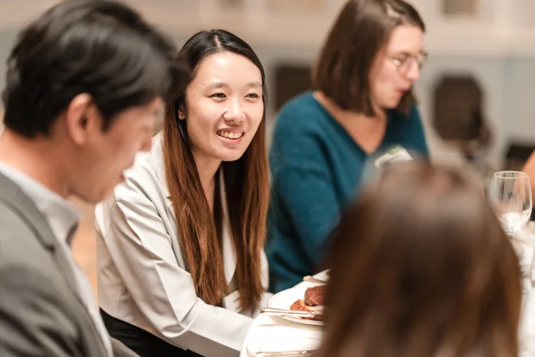 A guest smiling while seated with colleagues at the S-OIL European customer dinner.