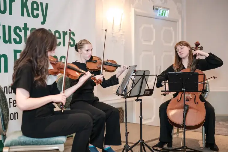 The string trio performing in front of the dinner sign at the S-OIL European customer dinner.