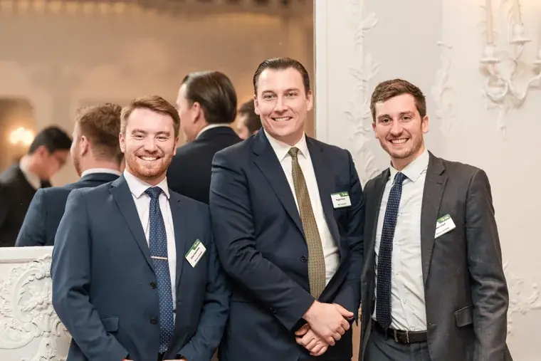 Three guests posing beside the event sign at the S-OIL European customer dinner.