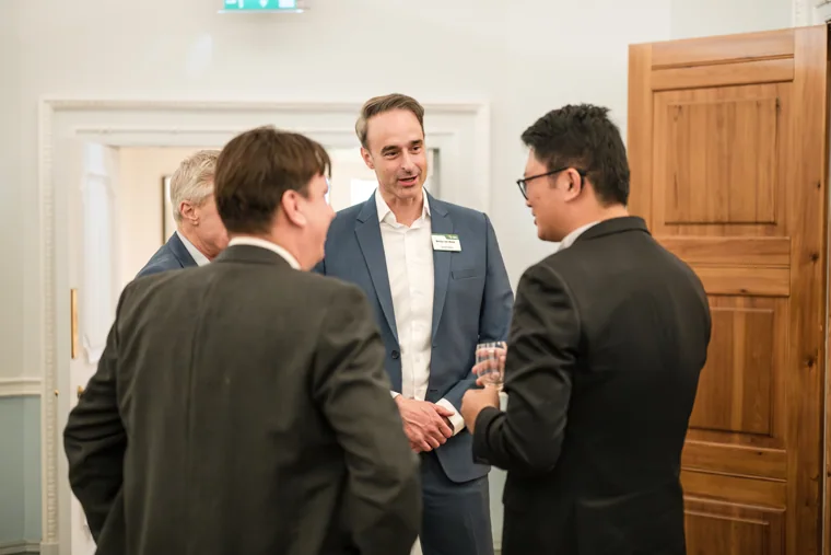 Three guests talking by a wood-panelled wall at the S-OIL European customer dinner.