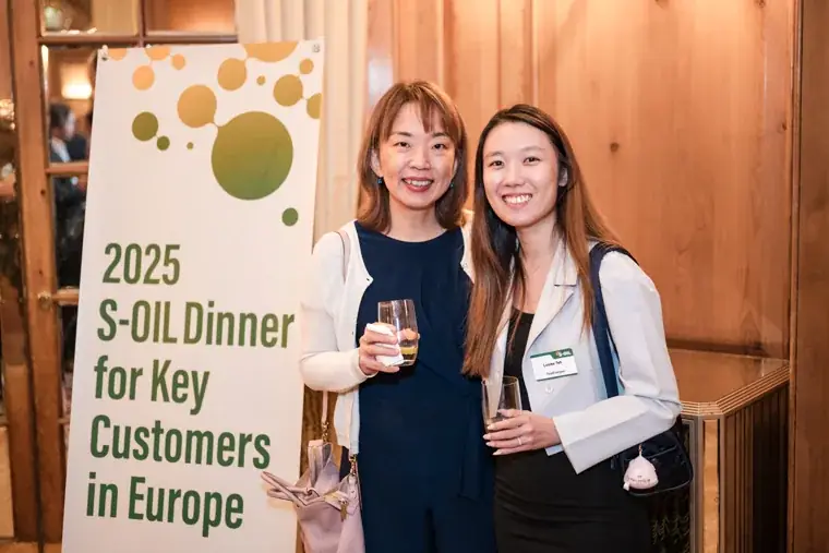 Two women posing in front of the event sign at the S-OIL European customer dinner.